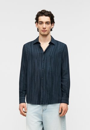 Marineblaues Langarmshirt mit vertikalen Streifen, Knopfleiste vorne und lockerem Kragen; hergestellt aus leichtem, strukturiertem Stoff.