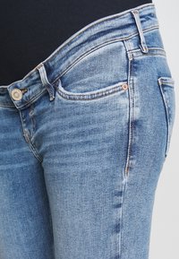 Vaaleansiniset farkut, joissa on tiivis siluetti, nappikiinnitys vyötäröllä, etutaskut ja hienovaraisia haalistumia kankaassa.