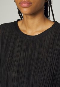 Top plissettato nero con scollo a costine. Tessuto leggero con una texture morbida. Il design presenta linee verticali e una silhouette aderente.