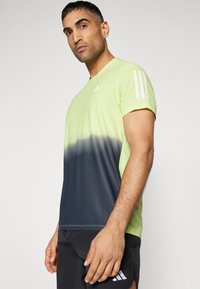 Camiseta deportiva en gradiente verde y azul marino, hecha de una tela ligera, con mangas cortas y tres rayas blancas en el hombro.