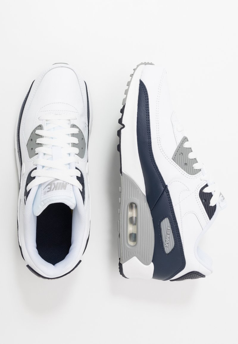 Zapatillas Nike Air Max 90 blancas con acentos en gris y marino, que cuentan con una parte superior de malla, cuello acolchado y amortiguación de aire visible en la suela.