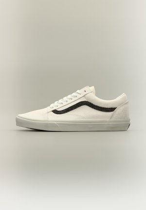 Baskets basses blanches avec des lacets blancs et une bande ondulée noire sur le côté, montrées de profil sur un fond neutre.