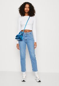 Camisola curta de manga longa branca com bainha desfiada, jeans retos azul claro, bolsa de ombro azul metálico e ténis cinzentos com detalhes.