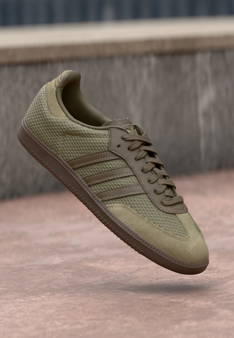 Olive green sneaker with mesh and suede materials, featuring three horizontal stripes, textured accents, and a flat rubber sole.