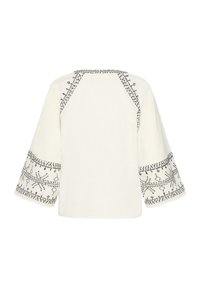 Blusa bianca con lunghe maniche raglan, caratterizzata da un intricato ricamo nero lungo le maniche e il colletto. Tessuto leggero e testurizzato.