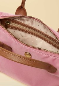 Borsa di tessuto rosa con manico marrone testurizzato e cerniera. All'interno, una fodera beige con pois bianchi e una tasca aggiuntiva con cerniera.