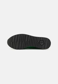 Black rubber shoe sole with horizontal grooves, featuring a circular pattern at the heel and a green outer edge.