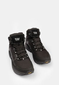 Crne planinarske čizme s teksturiranom površinom, s visokim dizajnom gležnja, vezicama, reflektirajućim detaljima i Vibram logom na potplatu.