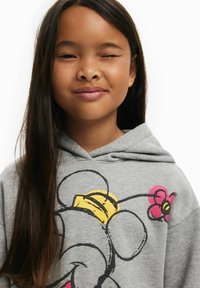 Sudadera gris con diseño de dibujos animados que presenta un elefante y una flor colorida. Textura suave, corte relajado y un bolsillo canguro frontal.