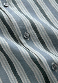 Gros plan d'un tissu rayé bleu et blanc avec trois boutons bleus cousus en ligne verticale.