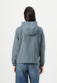 Lys grå hettegenser med elastiske mansjetter, avslappet passform og enkelt design, kombinert med blå denimjeans.