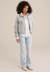 Chaqueta gris corta con dos bolsillos frontales, camisa blanca de botones, jeans de campana azul claro y zapatos blancos con suelas de goma. Textura suave.