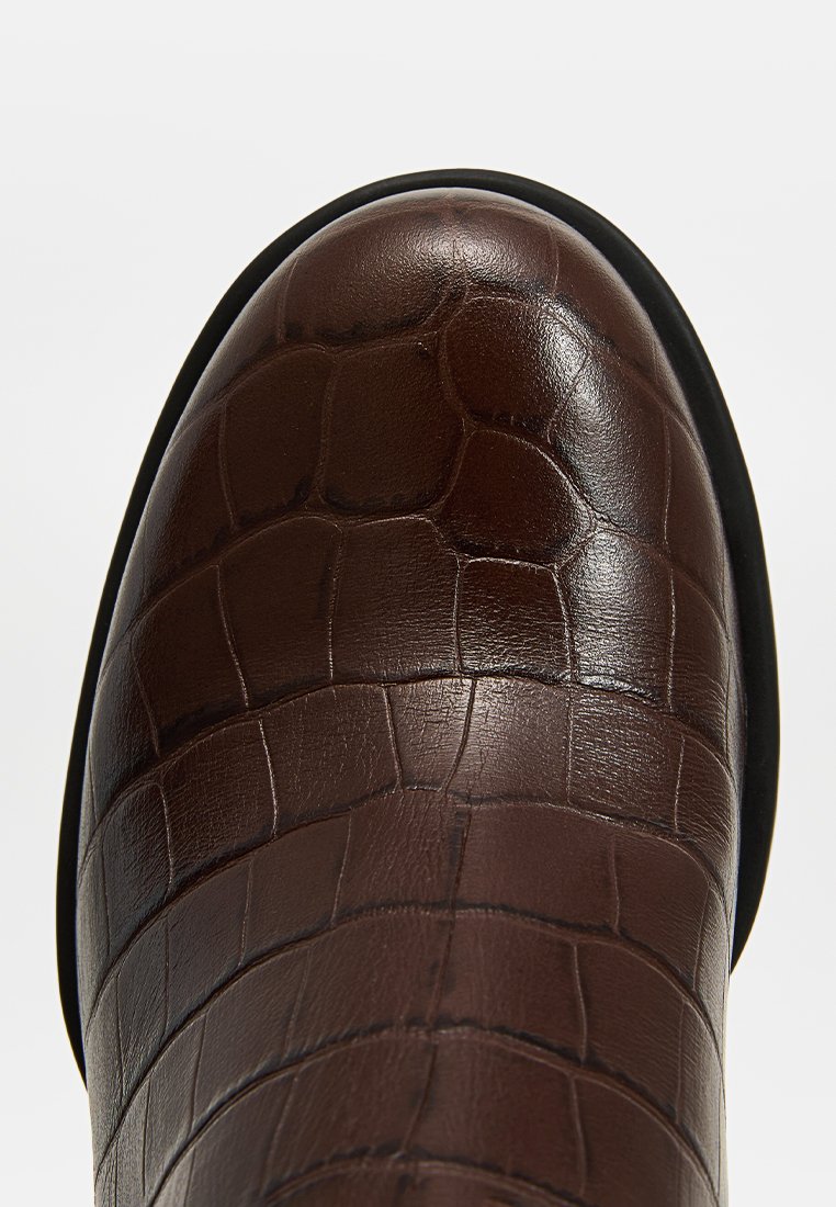 Stivale in pelle marrone con texture a stampa coccodrillo, punta tonda e suola in gomma nera. Focus su un dettagliato motivo e una finitura liscia.