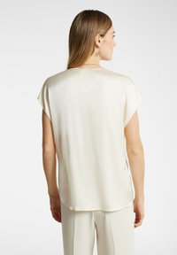 Top di raso beige chiaro con maniche corte, orlo curva e fessure laterali. Texture liscia e design semplice con una vestibilità ampia.