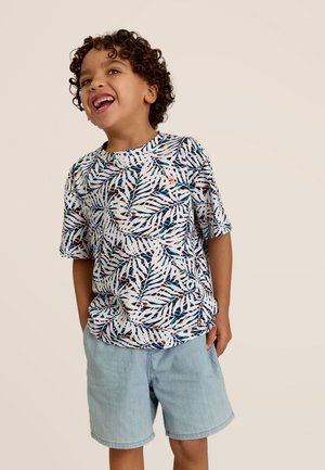 Chemise à manches courtes avec une base blanche présentant un motif de feuilles colorées. Assortie à un short en denim bleu clair. Tissu doux, coupe décontractée.