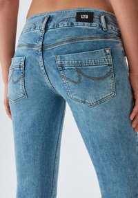 Jean en denim bleu clair avec taille mi-haute, poches arrière avec coutures décoratives et une étiquette noire portant les lettres "LTB."