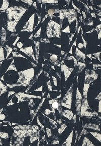 Marinblått och vitt mönstrat tyg med abstrakta former; inkluderar silverfärgade metallknappar och en strukturerad yta.