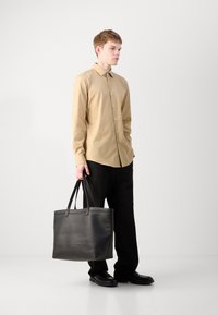 Cămașă bej deschis cu nasturi, geantă tote neagră cu textură netedă, pantaloni negri și pantofi. Design simplu, fără modele sau accente vizibile.