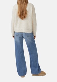 Beiger strukturierter Pullover mit geripptem Saum, kombiniert mit hellblauen weitgeschnittenen Jeans. Die Schuhe sind in einem sandfarbenen Ton mit glatter Textur.