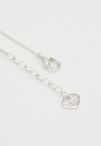 Collana in argento con grandi anelli, chiusura a moschettone e un charm a forma di cuore con dettagli incisi e finitura lucida.
