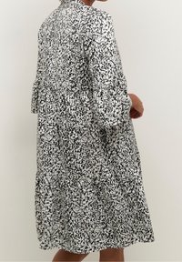 Robe à motifs noir et blanc avec une coupe décontractée, de légères volants aux manches et une taille froncée, fabriquée en tissu léger.