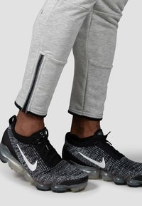 Sorte og grå Nike sneakers med en tekstureret strikket overdel og en gennemsigtig luftdæmpende sål; parret med lysegrå tapered bukser med lynlåse.