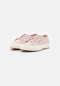 Paire de chaussures de sport montantes en toile rose clair avec semelles en caoutchouc blanc et étiquette du logo de la marque sur le côté, présentées sur un fond blanc.