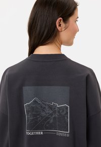 Felpa grigio scuro con stampa grafica di montagne e la parola "INSIEME" sul retro. Tessuto morbido, colletto rotondo, vestibilità rilassata.