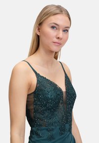 Smaragdgrünes Kleid mit einem taillierten Satinrock, der mit Spitze und Perlenverzierungen auf einem durchsichtigen Oberteil sowie verstellbaren Spaghetti-Trägern ausgestattet ist.