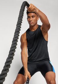 Black sleeveless athletic shirt and fitted shorts with a blue accent. The person grips a thick, dark battle rope, showing defined arm muscles.