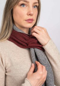 Tørklæde i bordeaux og grå uldblanding, med et tekstureret design og lagdelt drape omkring halsen, parret med en lys beige sweater.