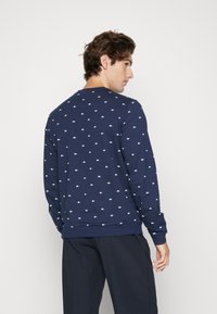 Navy blue sweatshirt with small white logo pattern, crew neckline, long sleeves, textured fabric, and ribbed cuffs and hem.