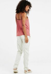 Top rosso senza maniche con una vestibilità morbida e spalline sottili, abbinato a pantaloni cargo beige chiaro. L'outfit ha una texture liscia.