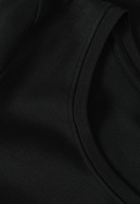 Tissu de T-shirt noir montrant une texture lisse, un col rond et des coutures visibles. Le matériau semble extensible et léger.