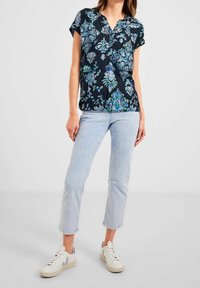 Svart topp med blommönster i blå och gröna nyanser. Korta ärmar och design med v-ringning. I kombination med ljusblå jeans och vita sneakers.