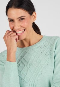 Maglione lavorato a maglia verde menta chiaro con modelli geometrici testurizzati e dettagli in pizzo sul davanti e sulle maniche.