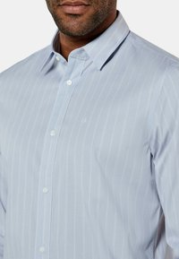 Camicia azzurro chiaro con colletto, caratterizzata da sottili righe bianche, chiusura con bottoni sul davanti e un sottile logo "ck" sul lato sinistro. Tessuto testurizzato con finitura liscia.