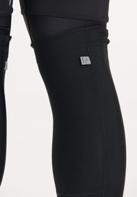 Kraftiga svarta träningsleggings gjorda av stretchigt material, med platta sömmar och en liten etikett märkt "HÖGER" nära knäområdet.