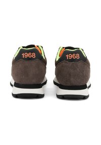 Une paire de baskets en daim marron avec un revêtement néon vert et "1968" en orange sur les languettes noires au talon, vues de l'arrière.