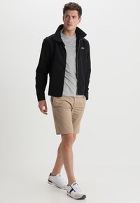 Black zip-up jacket with high collar, gray t-shirt, beige shorts, and white sneakers. Simple design with a subtle logo detail on the jacket.