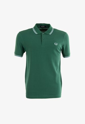 Polo verde de algodón con una apertura de dos botones, ribete blanco en el cuello y las mangas, y un pequeño logo bordado en el pecho.