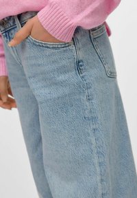 Jasnoniebieskie dżinsy o luźnym kroju, z kieszenią i subtelnym, teksturowanym wzorem, w zestawieniu z różowym swetrem z dzianiny.