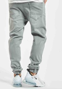 I pantaloni jogger grigi chiari presentano una vestibilità rilassata, polsini elasticizzati e due tasche posteriori. Abbinati a scarpe da corsa bianche e nere.