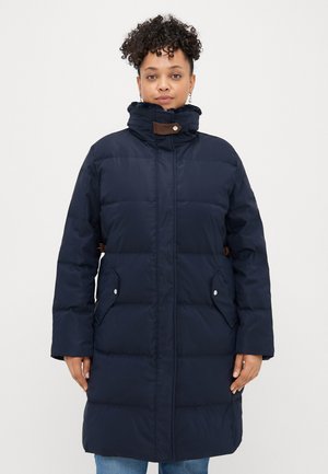 Abrigo de plumas navy con cuello alto, cierre de botones, bolsillos laterales y acentos marrones contrastantes. Textura suave y acolchada, diseño hasta la rodilla.