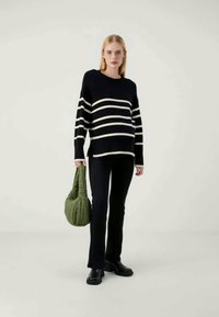 Prugasta pletena jopica v mornarici in krem, v kombinaciji s črnimi širokimi hlačami in zeleno prešito torbico. Gladka textura in sproščen kroj.