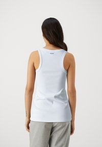 Débardeur en coton blanc avec une coupe ajustée et de larges bretelles, présentant un petit logo "HUGO" au dos. Texture lisse.