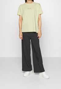 Světlounce žluté bavlněné tričko s krátkými rukávy, kulatým výstřihem a potiskem na hrudi. Kombinováno se širokými černými kalhotami a bílými teniskami.