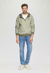 Groene pullover hoodie met een rits, twee voorkruiszakken en geribde manchetten. Draag het met lichtblauwe jeans en beige sneakers.