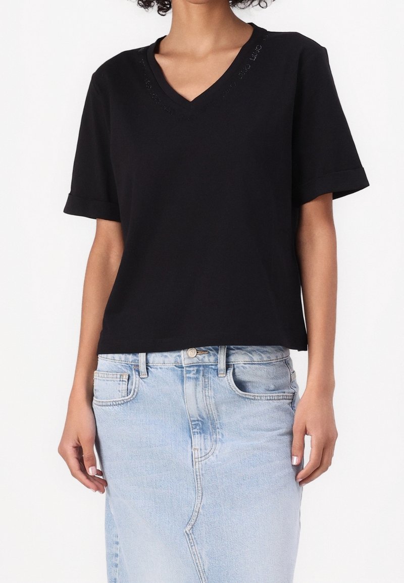 Femme portant un t-shirt noir à manches courtes et col en V, rentré dans une jupe en denim bleu clair avec des poches avant.