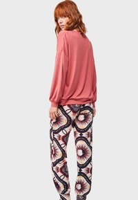 Camiseta larga de color rosa oversized, combinada con pantalones jogger de color crema con un patrón de diseños geométricos en rojo, negro y amarillo.